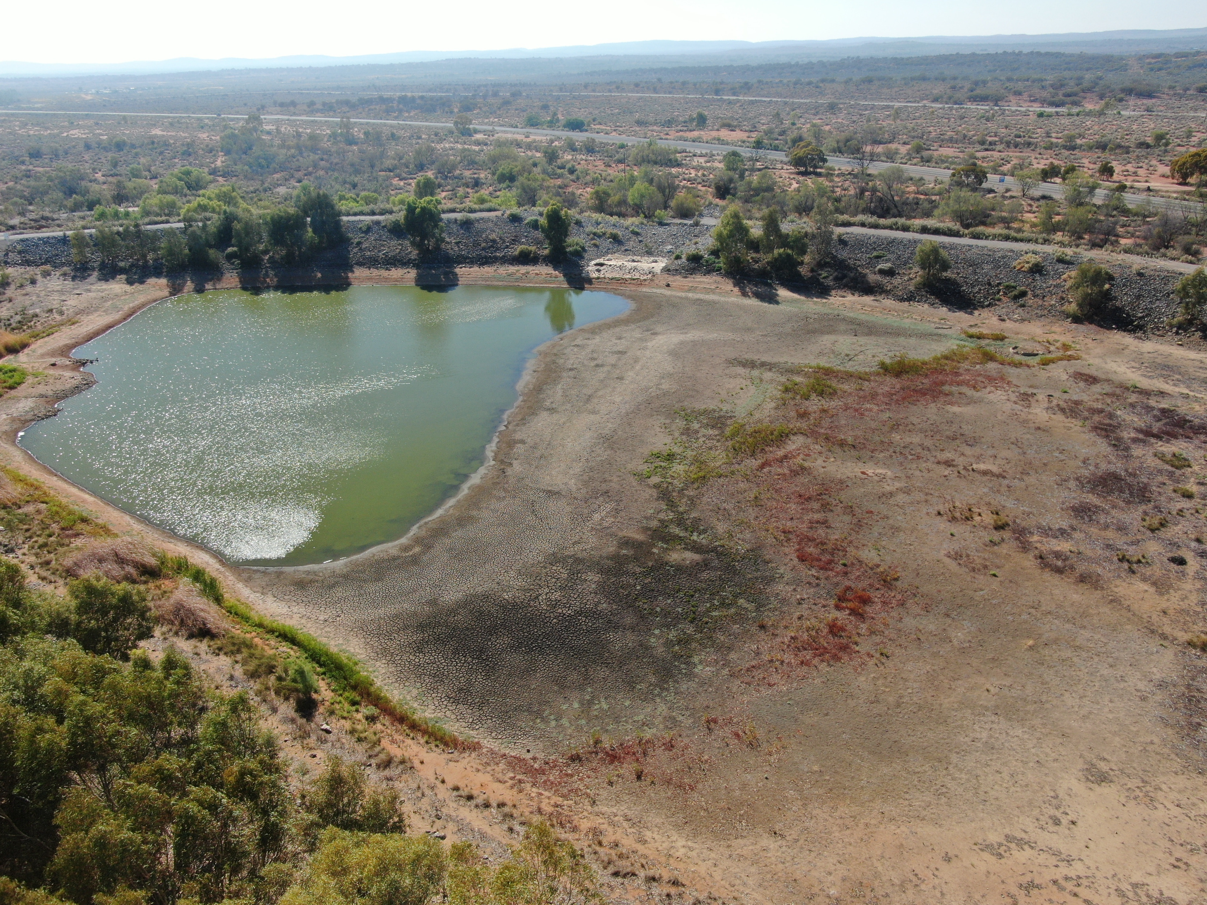 Uma ampla foto aérea de um pequeno corpo de água que secou para revelar uma extensão de leito de lago esparso e rachado.