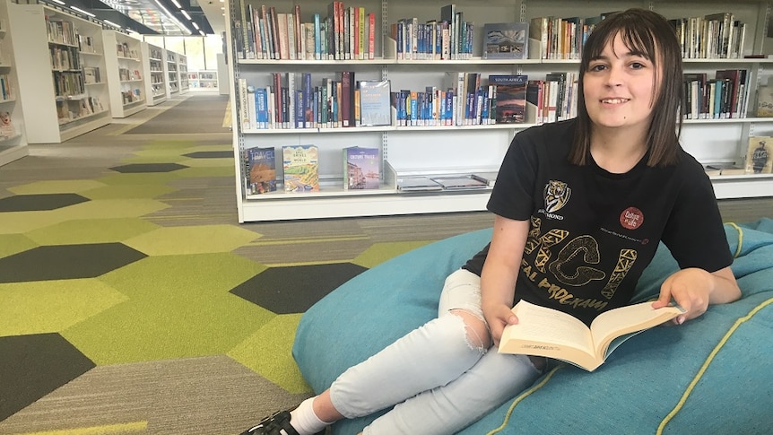Young woman sits on bean bag in a library with a book in her hands