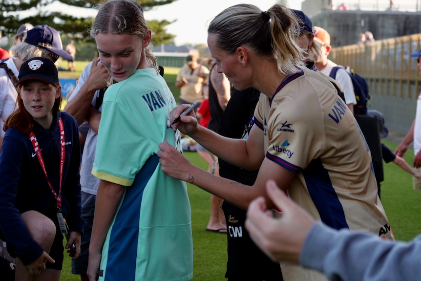 A female soccer player signs a fan's jersey.