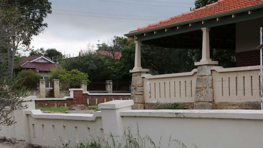 A house with a concrete fence that is leaning over.