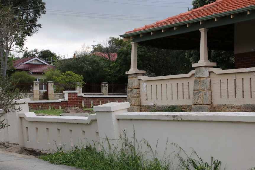 A house with a concrete fence that is leaning over.