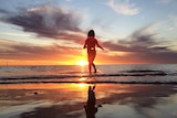 A child plays on the beach as the sun sets.