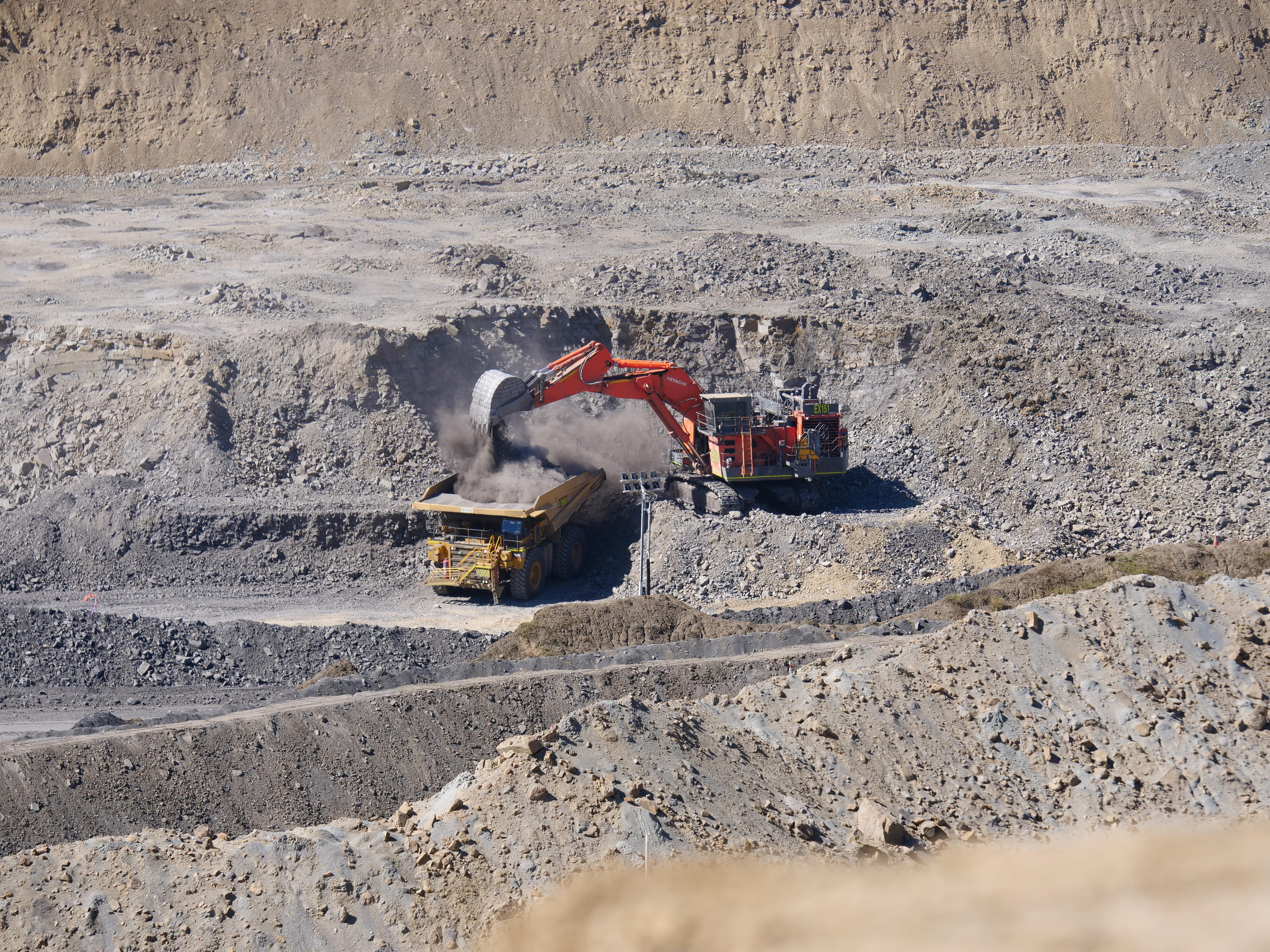Un gran camión volquete lleno por una excavadora, en medio de un pozo abierto de carbón. 