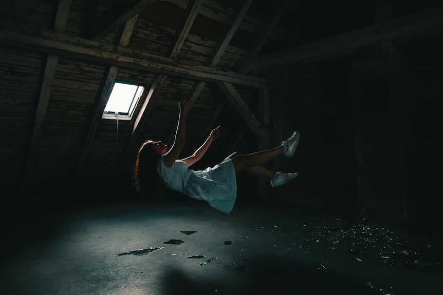 A woman in a white dress falling in a dark attic