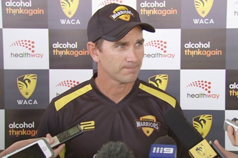 Justin Langer speaks to journalists wearing a Western Warriors shirt and hat.
