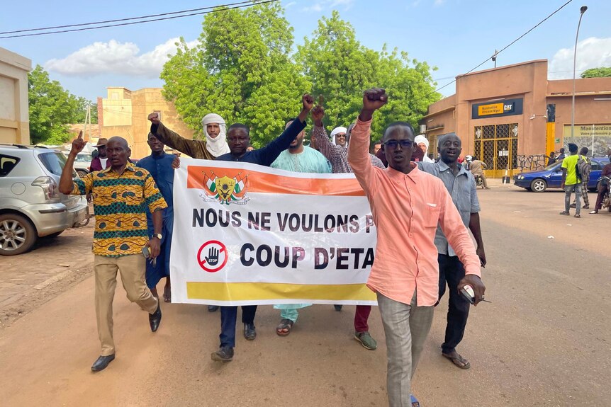 A group of men holding a banner with french text saying we don't want a coup with their fists in the air
