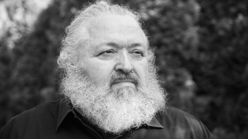 A black and white close up portrait of Bruce Mau shows him gazing into the distance with a thick white beard.