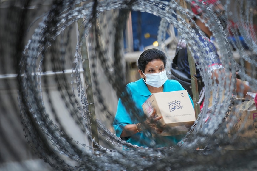 A resident wearing a face mask collects her package behind barbed wire