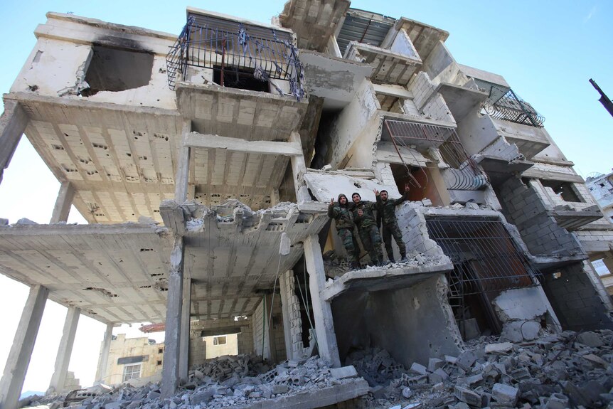 Members of the Syrian pro-government forces pose for a picture in a destroyed building.