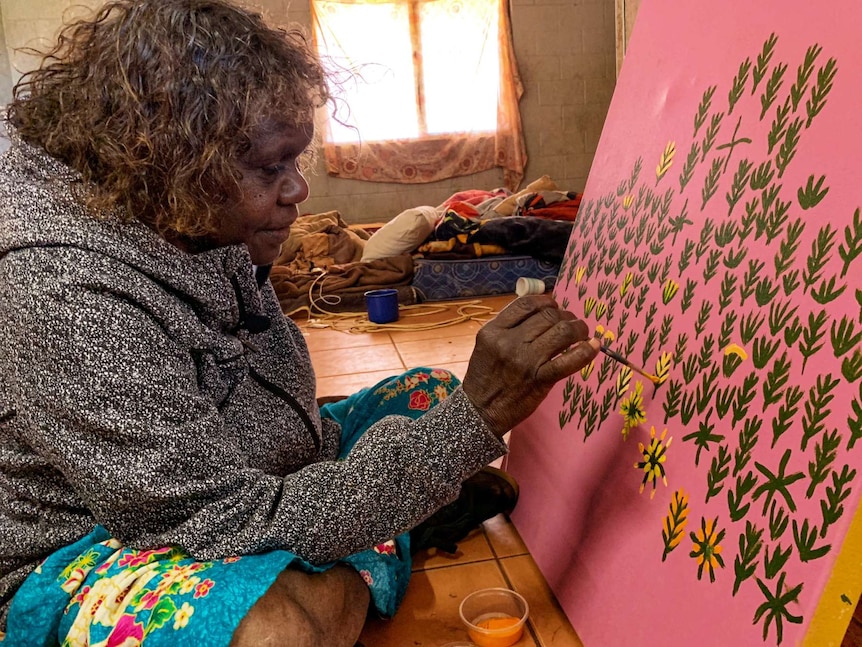 A woman sits on the floor painting.