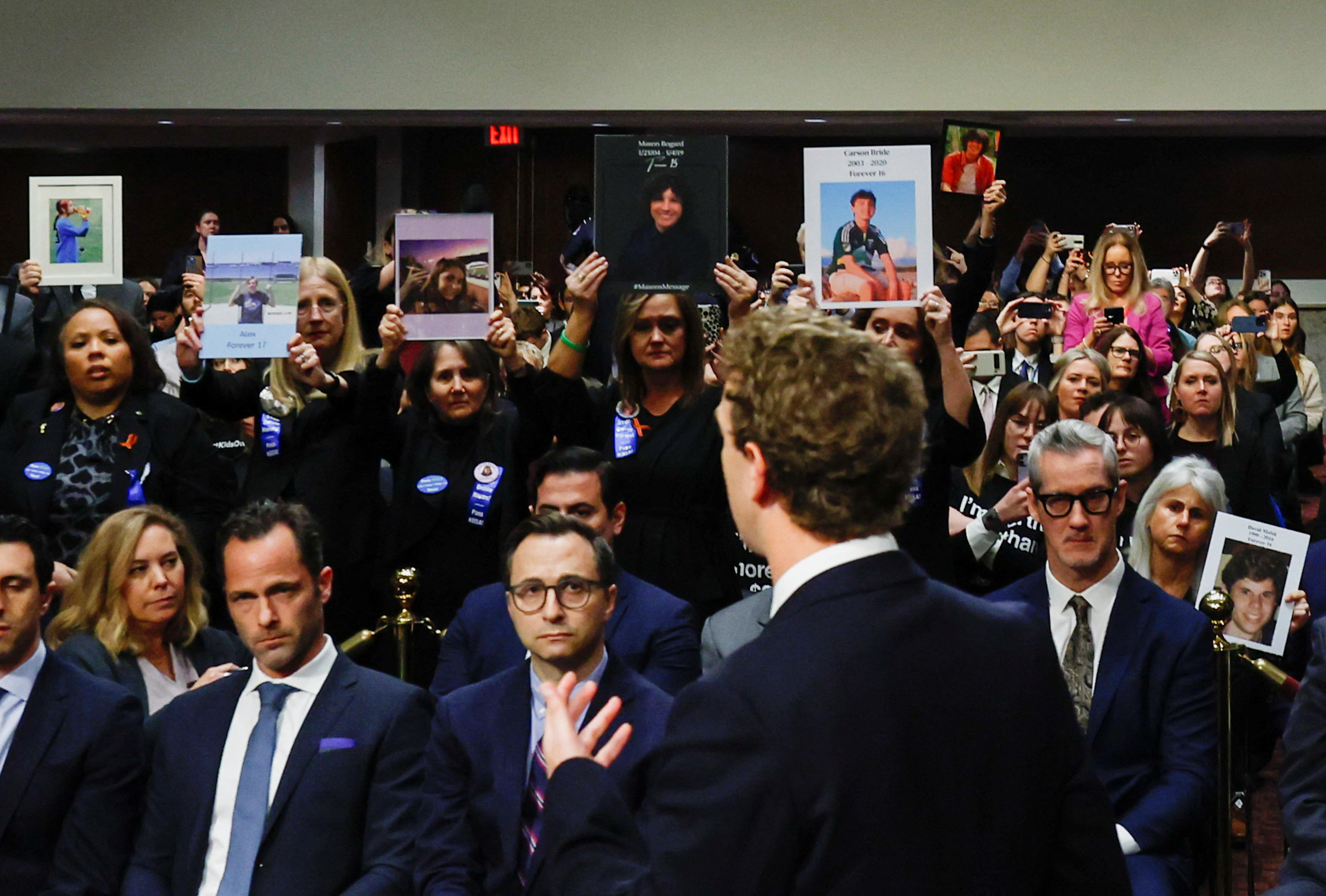 The back of a mans head standing in front of a crowd of people holding up placards of pictures