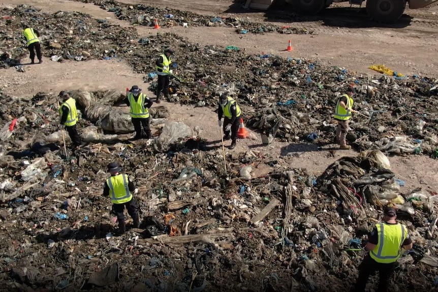 Police in hi-vis vests search through rubbish. 