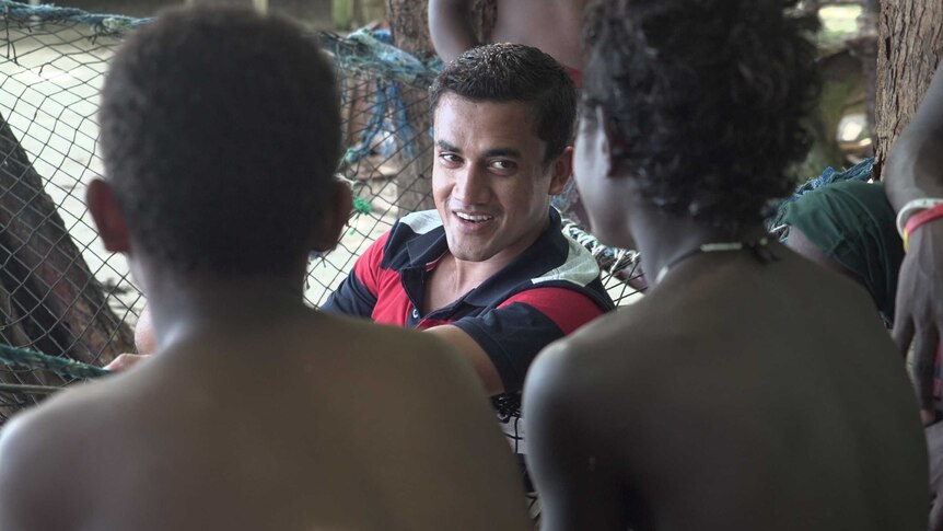 A man in a hammock speaks to people with their back to the camera.