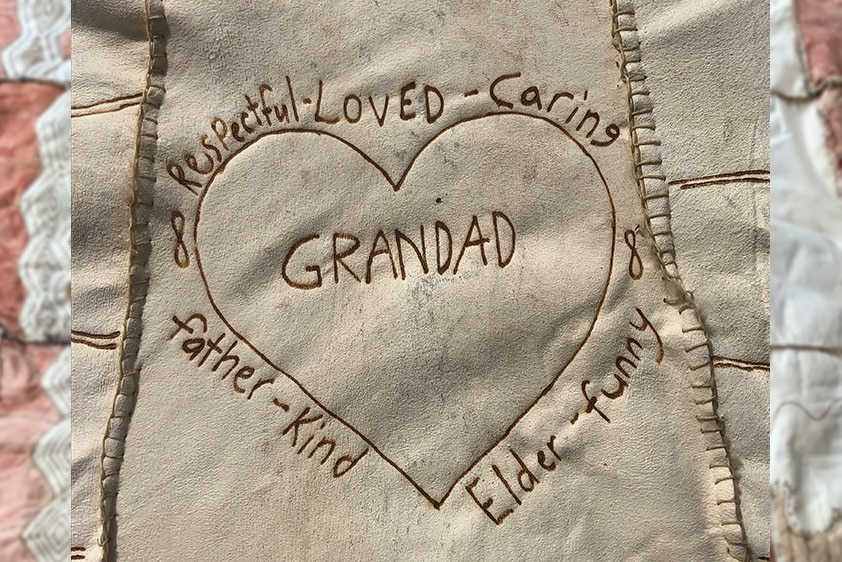 Close up of a heart and text "Grandad, respectful, loved, caring Elder", burnt into a the skin of a possum and sewn into a cloak