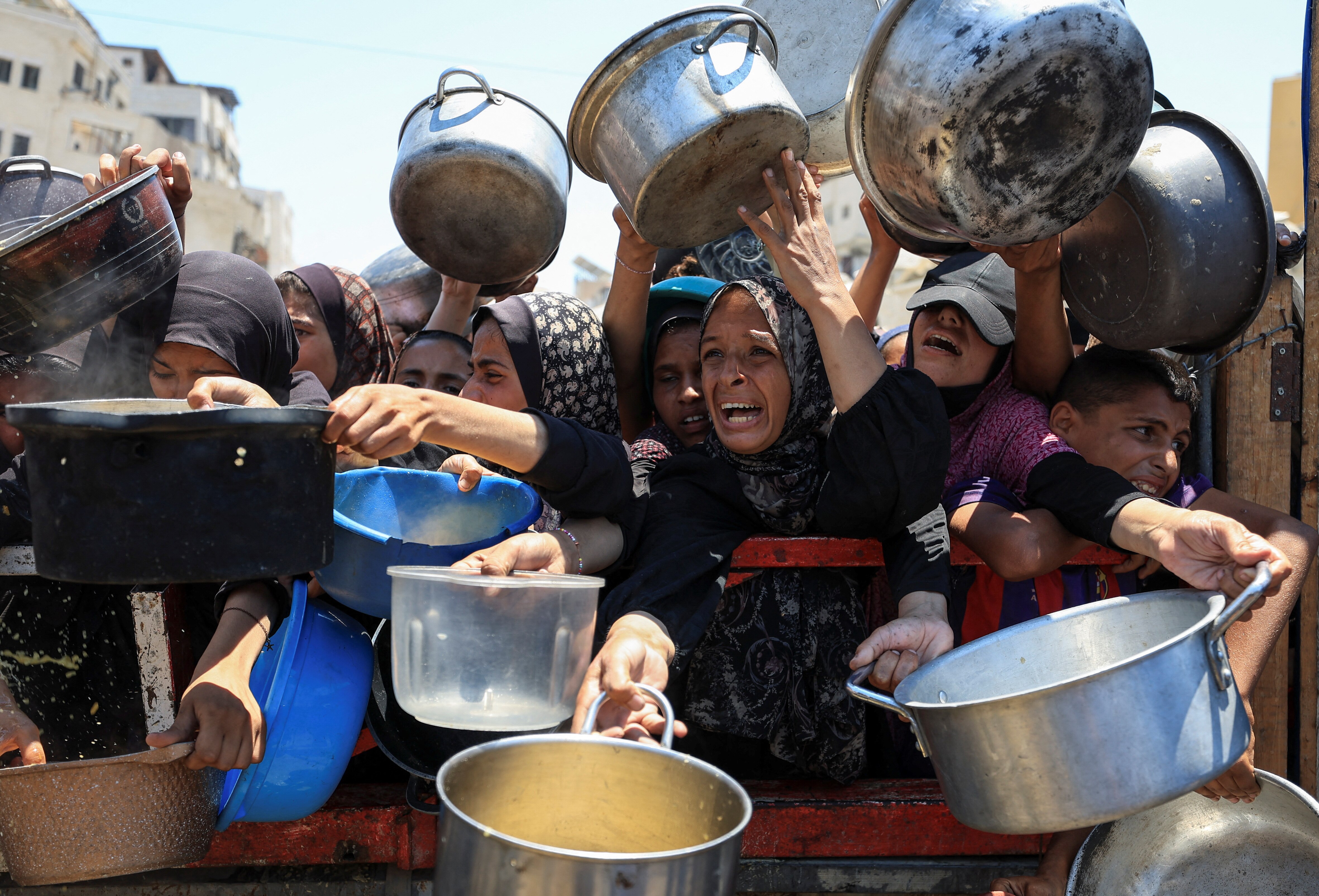 palestinian women hold pots begging for food at an aid site in gaza