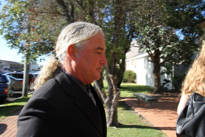 A man in a black suit with long white hair