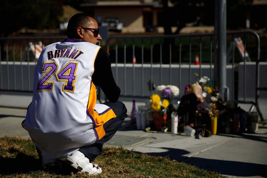 A man wearing a Kobe Bryant jersey crouches as he looks at floral tributes laid near the helicopter crash site.