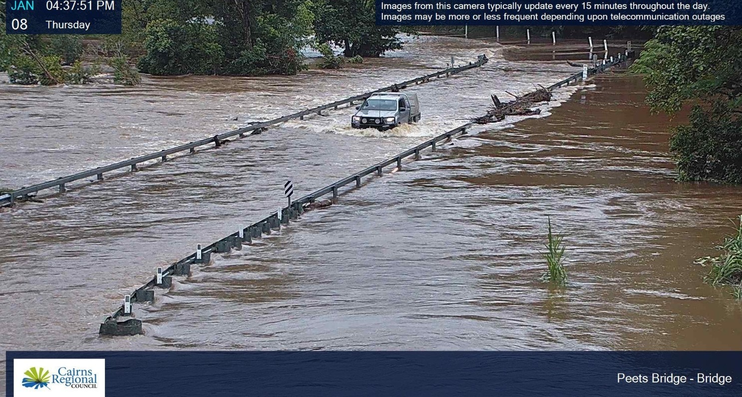 Una ute fue captada por la cámara conduciendo a través de un puente inundado: el camino está cubierto y el agua se derrama sobre los neumáticos de la ute.