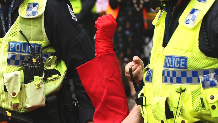 An Extinction Rebellion dressed in red being carried away by several police.