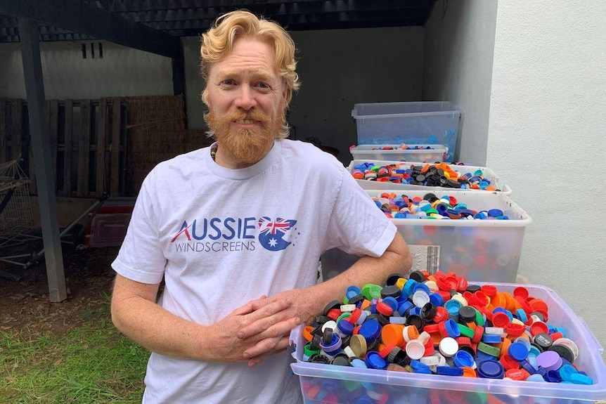 Tim Miller, stands next to a wall of plastic tubs, full of plastic lids.