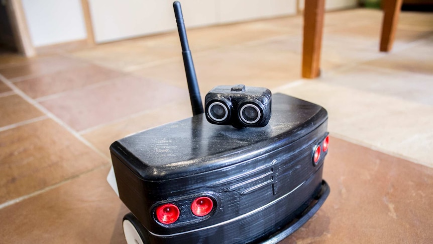 A black robot, the size of a tissue box, with a bus-like front and a small head with two large eyes