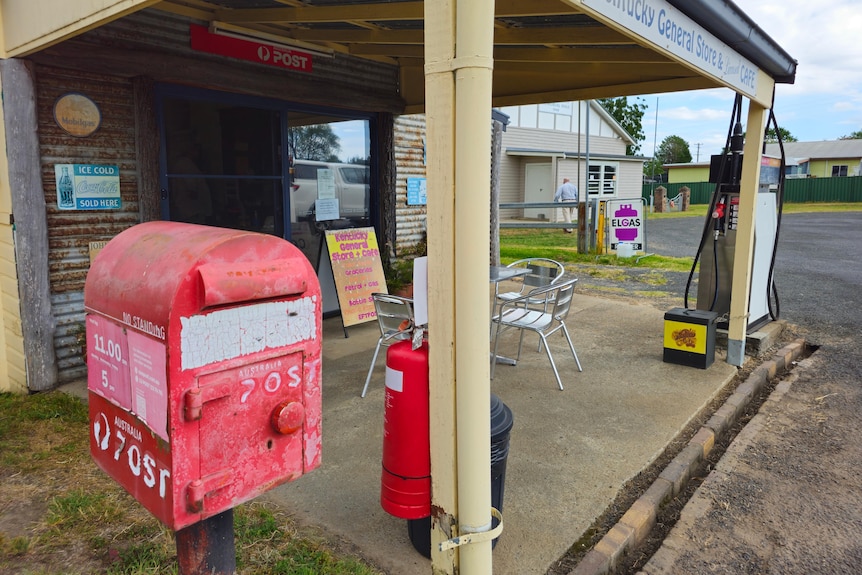 A post box and fuel bowser under a porch in a empty street.
