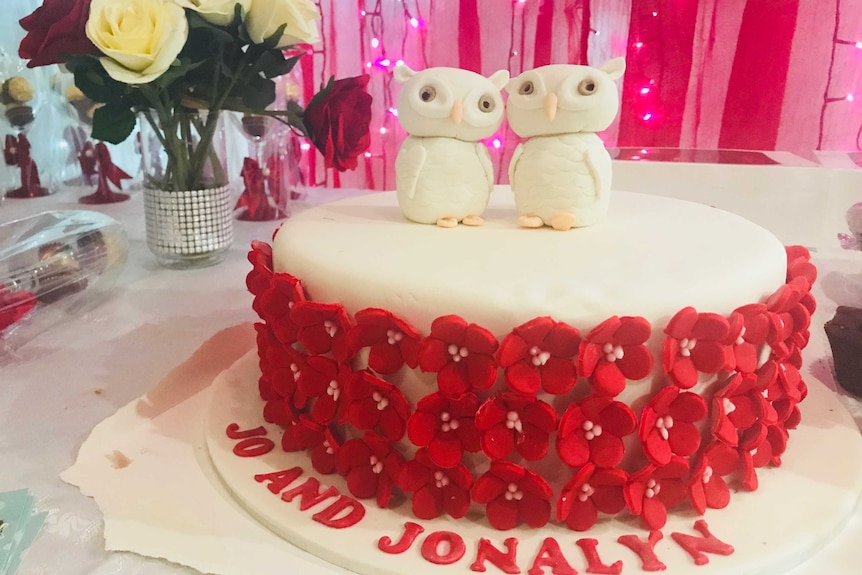 A wedding cake with two white owls on top, and red flowers around the sides.