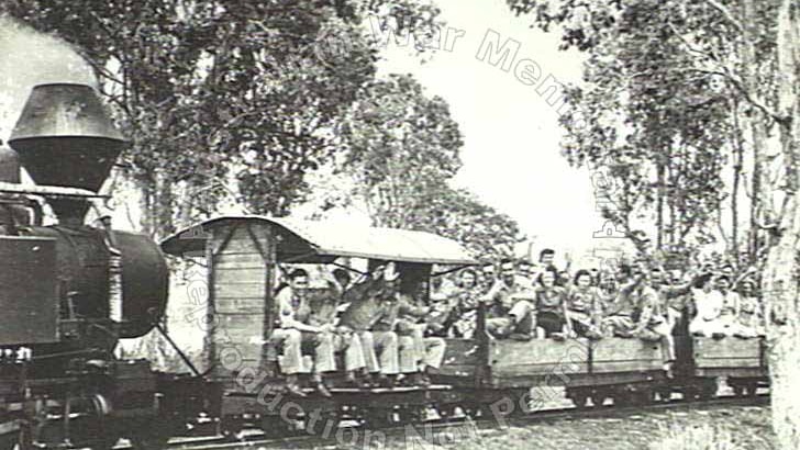 A black and white photo of a group of about 20 men and women on a cane train smiling