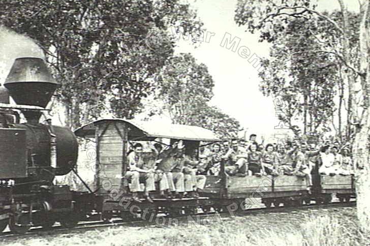 A black and white photo of a group of about 20 men and women on a cane train smiling