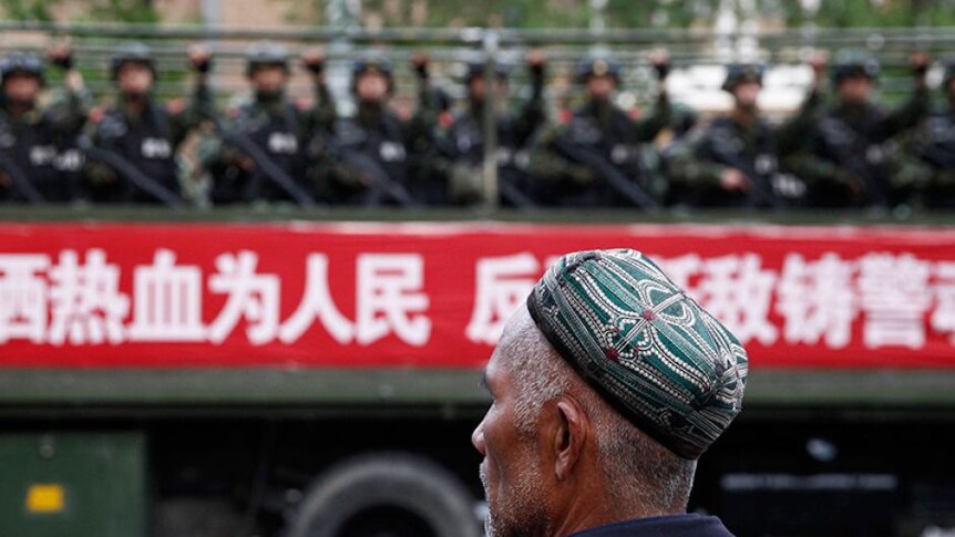 Pria Uyghur melihat sebuah truk yang membawa polisi paramiliter yang bertugas di jalanan selama aksi anti-terorisme di China.