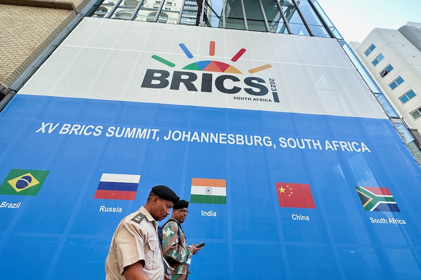 People walk past a convention centre with a large billboard advertising the BRICS summit with flags of each country.