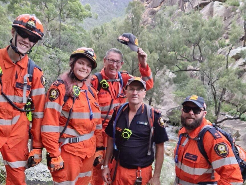 A group of SES volunteers dressed in orange taking a selfie in front of a mountain range