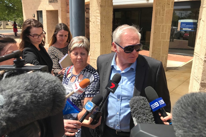 Jim and Catherine McDougall surrounded by media speak into microphones in front of the Busselton court house.
