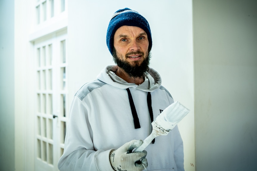 A painter all in white holding a paintbrush.