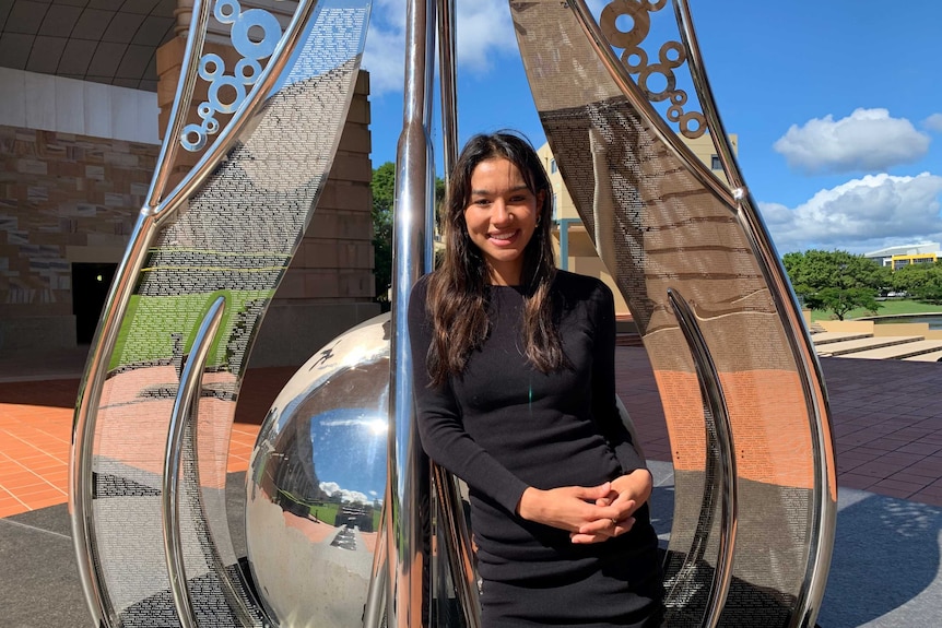 Graduate Veronica McNevin beside a steel globe sculpture at Bond University campus Gold Coast