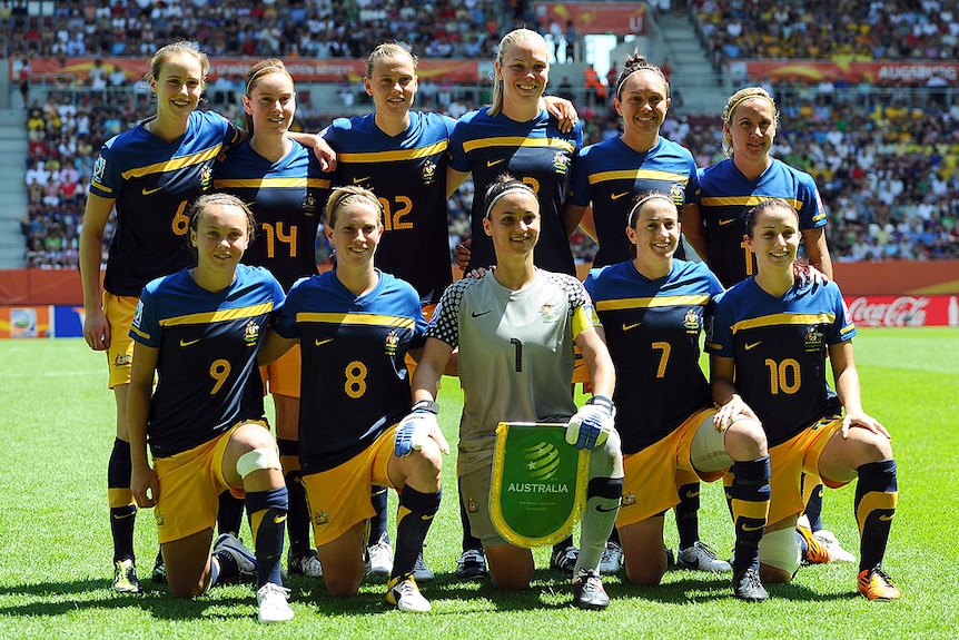 A women's soccer team wearing yellow and blue poses for a photo before a game
