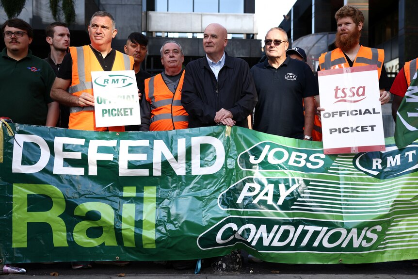 A group of workers with a sign which reads Defend Rail Jobs Pay Conditions