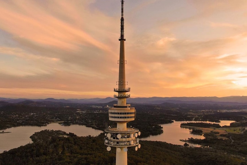 Telstra Tower in the foreground overlooking Lake Burley Griffin with the sun setting over mountains.