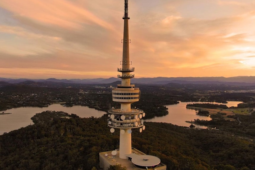 Telstra Tower in the foreground overlooking Lake Burley Griffin with the sun setting over mountains.