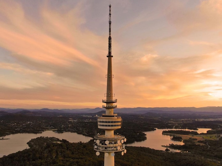 Telstra Tower in the foreground overlooking Lake Burley Griffin with the sun setting over mountains.