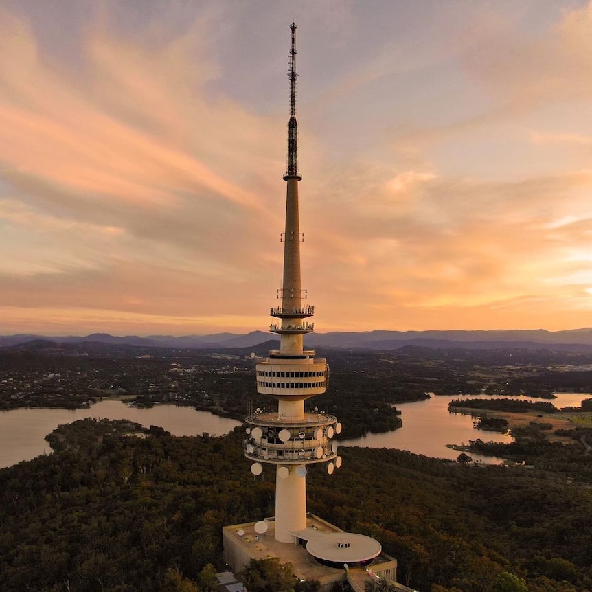 Telstra Tower in the foreground overlooking Lake Burley Griffin with the sun setting over mountains.