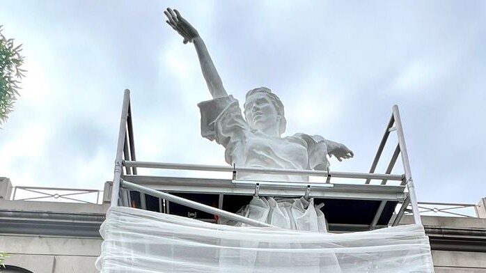 Photo of a female statue with scaffolding around he. There is fabric draped over the scaffolding.