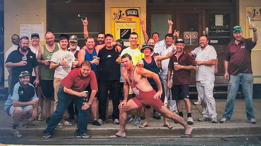 A bunch of men pose for a photo on the street in front of the pub. They look happy.