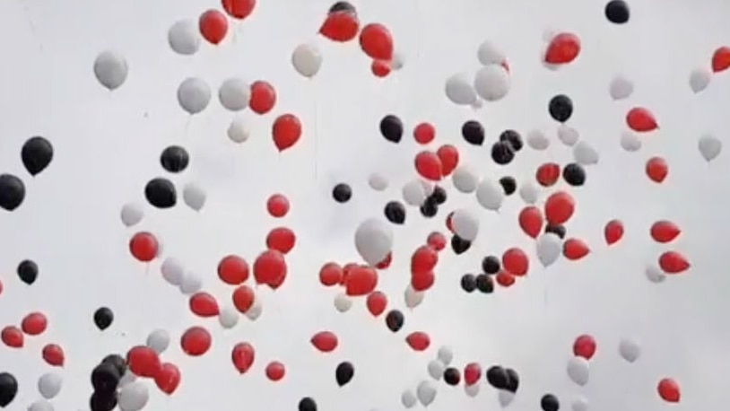 Red, black and white balloons floating against a grey sky.