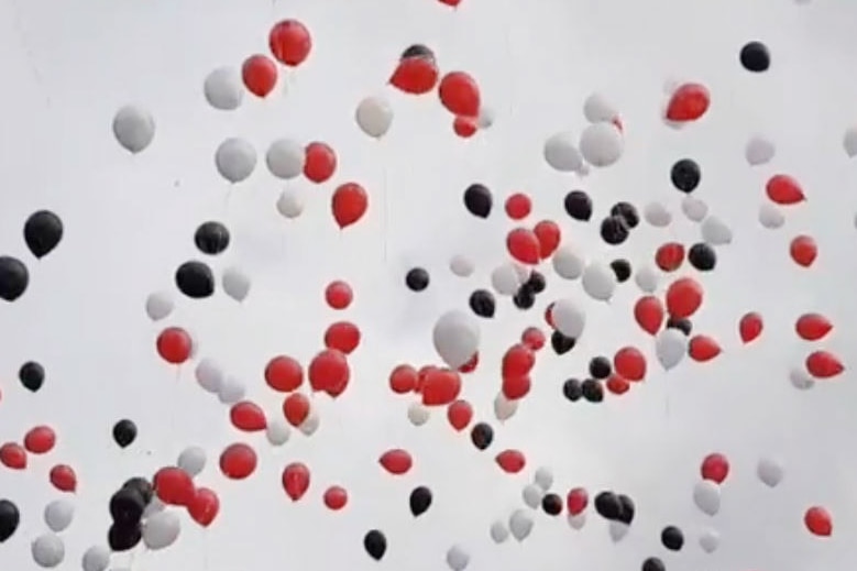 Red, black and white balloons floating against a grey sky.