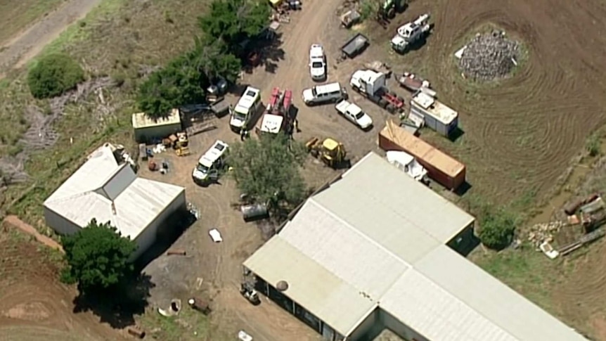 An aerial shot of a number of emergency vehicles parks outside a farm building.