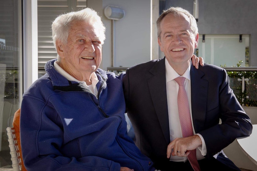 Bob Hawke wearing a purple jumper and Bill Shorten in a dark suit and light coloured tie smile at the camera