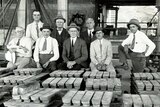 Men stand behind piles of lead bullion.