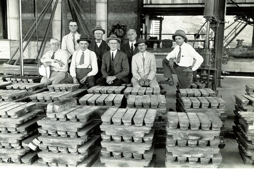 Men stand behind piles of lead bullion.