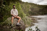 Arpit Charwal sits on a rock by a river, surrounded by bushland.